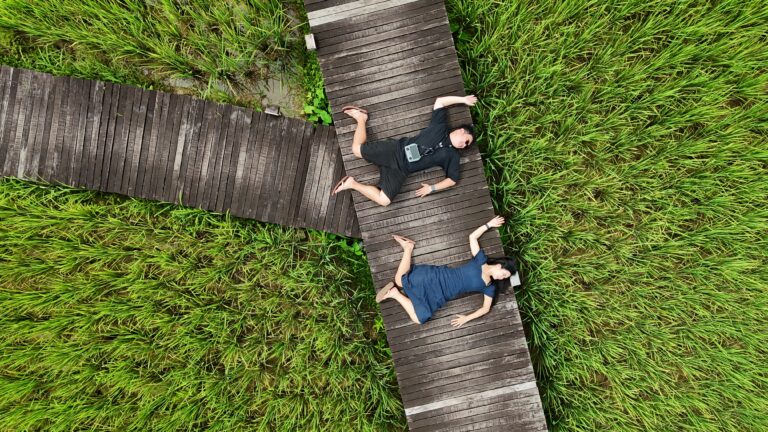 Couple lying on a wooden boardwalk in rice fields at ViengTara Vangvieng Resort, Vang Vieng, Laos