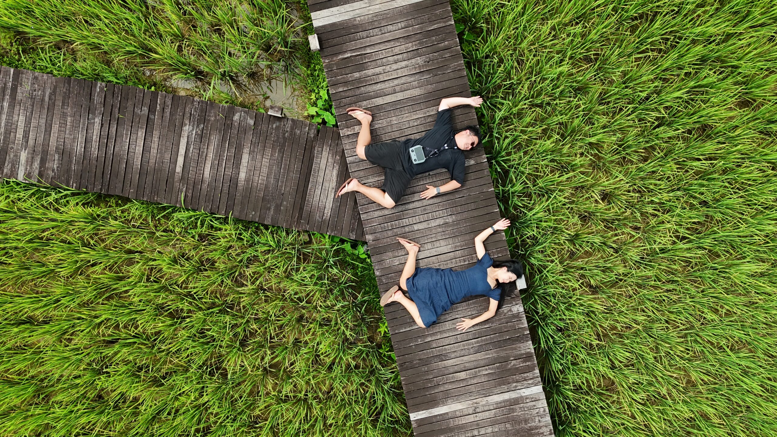Couple lying on a wooden boardwalk in rice fields at ViengTara Vangvieng Resort, Vang Vieng, Laos